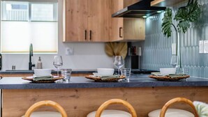 A modern kitchen with wooden cabinets, a dark countertop, and three wicker chairs with white cushions.