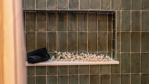 A bathroom with a tiled wall, a shelf with towels, and a small window with flowers.