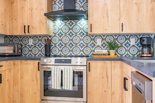 A kitchen with wooden cabinets, a stove, a coffee maker, and a patterned backsplash. - Quaint Studio in Charming Marston Hills (San Diego)