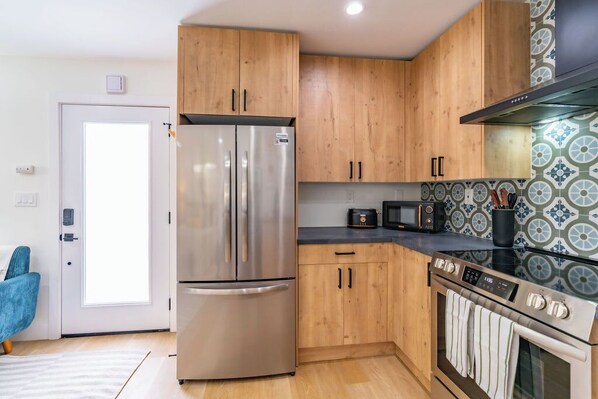 A modern kitchen with wooden cabinets, stainless steel appliances, and patterned backsplash tiles. - Quaint Studio in Charming Marston Hills (San Diego)