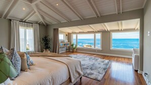 A bedroom with a large bed, a view of the ocean, and a ceiling with exposed beams. - Dolphin's Paradise Su (San Diego)