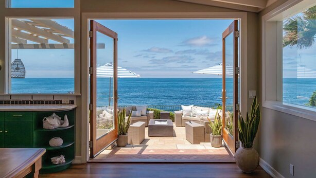 A room with a view of the ocean, a patio area with outdoor furniture, and a green cabinet with decorative items. - Dolphin's Paradise Su (San Diego)