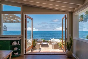 Une pièce avec vue sur l’océan, un patio aménagé avec du mobilier d’extérieur et un meuble vert contenant des objets décoratifs.