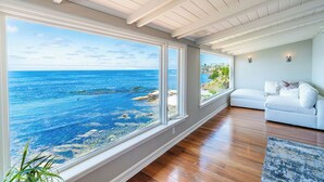 A room with large windows overlooking the ocean, a white sofa, and wooden flooring. - Dolphin's Paradise Su (San Diego)