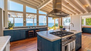 A modern kitchen with a large island, built-in appliances, and large windows offering ocean views. - Dolphin's Paradise Su (San Diego)