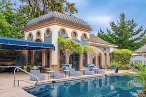 Un espace aménagé au bord de la piscine, avec des chaises longues, une piscine et un bâtiment doté d’un dôme et de fenêtres en arc de cercle.