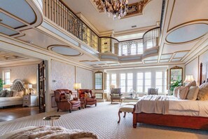 Une pièce spacieuse comprenant un grand lit, deux fauteuils, un canapé et une table à manger. Un escalier avec une balustrade mène à un niveau supérieur.