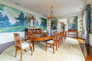 A dining room with a large oval table, wooden chairs, a chandelier, and a large landscape painting on the wall. - Fox Hill Manor, A Masterpiece Estate (San Diego)