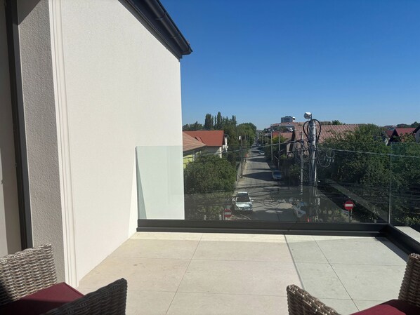 A balcony with a glass door, wicker furniture, and a view of a street with houses and a clear sky.