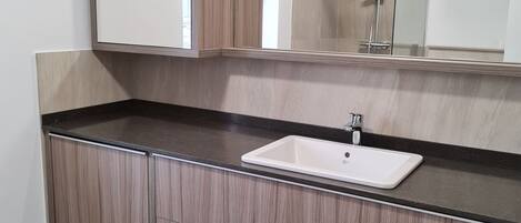 A modern bathroom with a wooden vanity, a white sink, and a large mirror above the vanity.