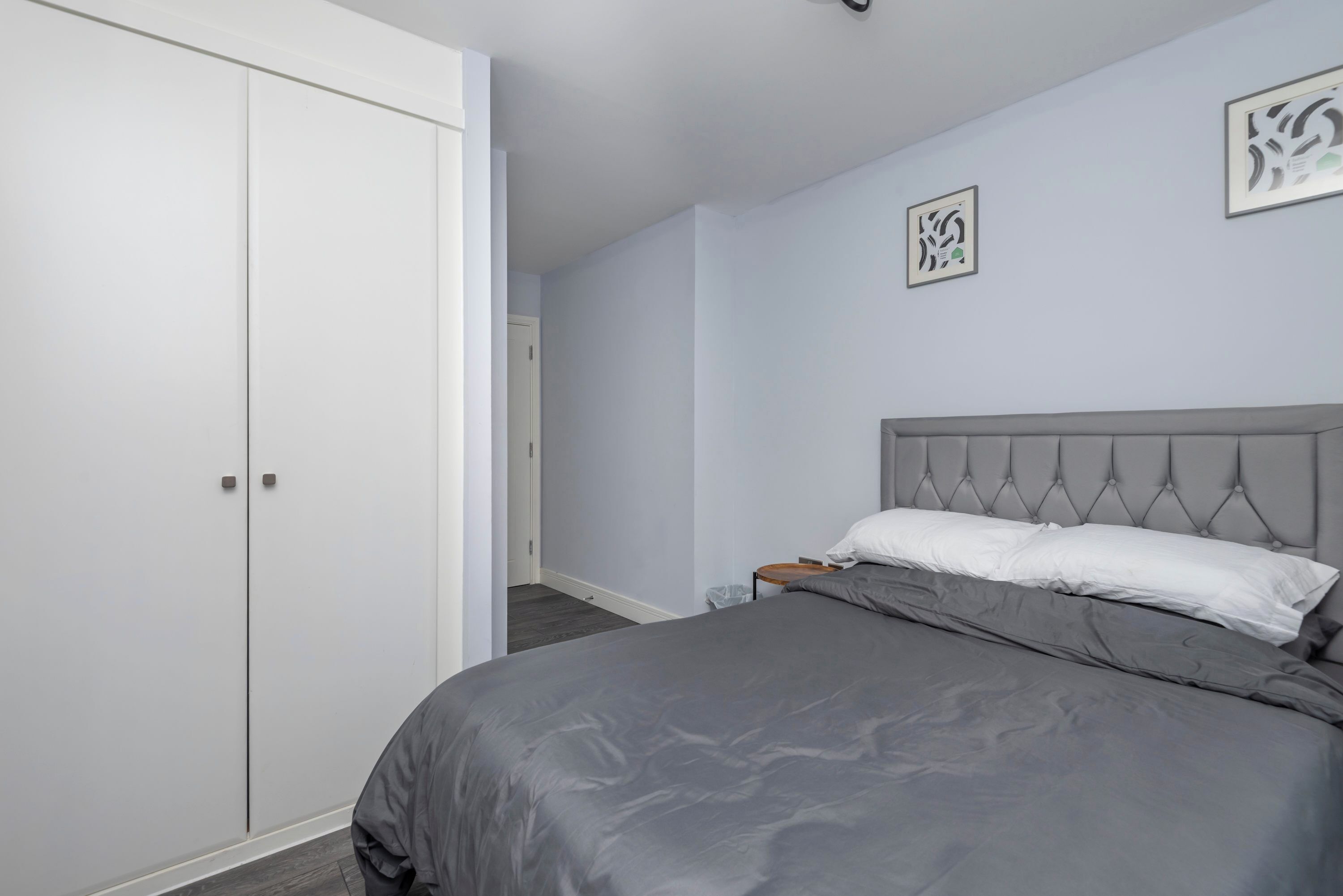 A bedroom with a bed, a wardrobe, and two framed pictures on the wall.