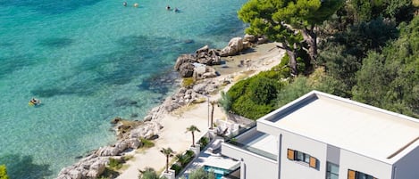 A coastal property with a swimming pool, a beach, and a view of the sea.