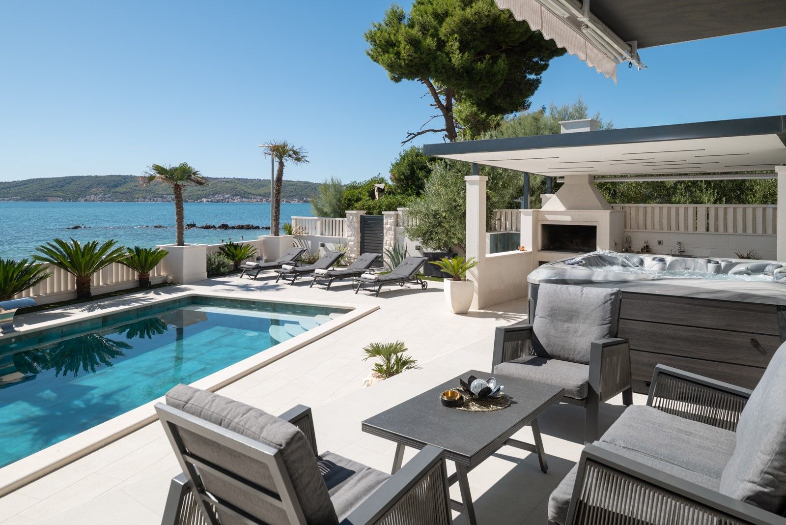 Un espace aménagé au bord de la piscine, comprenant un jacuzzi, des chaises longues et une vue sur la mer.