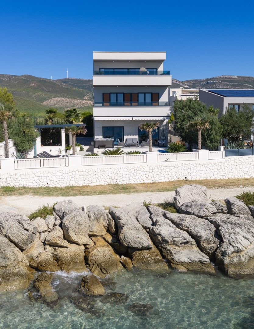 Ein modernes, zweistöckiges Gebäude mit einer Steinwand im Vordergrund und freiem Blick auf das Meer.