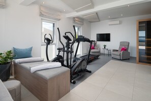 A modern living room with a sofa, exercise equipment, a TV, and a view of the outdoors.