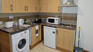 A compact kitchen with wooden cabinets, a microwave, a toaster, a sink, and a washing machine. - Primely Located 1-bed Apartment in Brighton (Brighton)