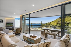 Ein modernes Wohnzimmer mit einem großen Glasschiebetür zu einem Balkon mit herrlichem Seeblick und Hügeln.