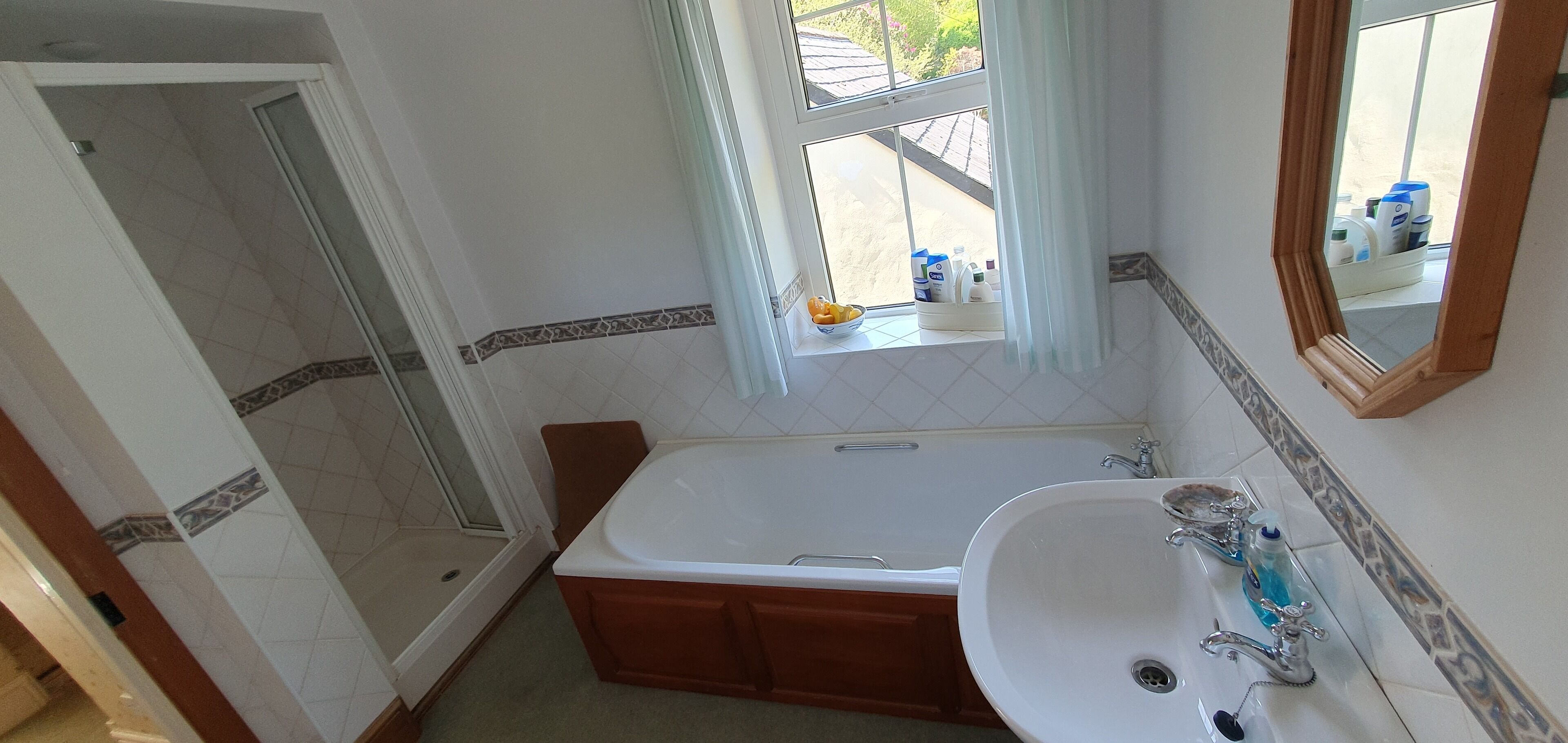 A bathroom with a bathtub, a sink, a shower, and a window with curtains.