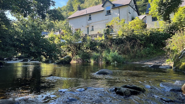 Una casa frente a un río, rodeada de árboles.