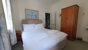 Una cama bien hecha con ropa blanca y una toalla doblada, un armario de madera y un cuadro en la pared.