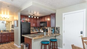 Una cocina con armarios de madera, un refrigerador negro, una encimera de granito y dos taburetes azules.