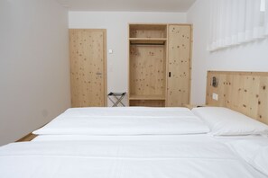 Un dormitorio con cama, armario de madera y una pequeña silla plegable.