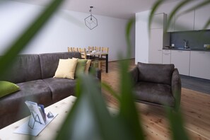 A modern living room with a grey sofa, a wooden dining table, and a kitchen area with white cabinets and a black countertop.