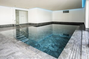 An indoor swimming pool with a clear water surface, a glass railing, and a tiled floor. - Chasa Helvetia Quatter: newly built 2.5-room holiday flat with exclusive hotel service (Müstair)