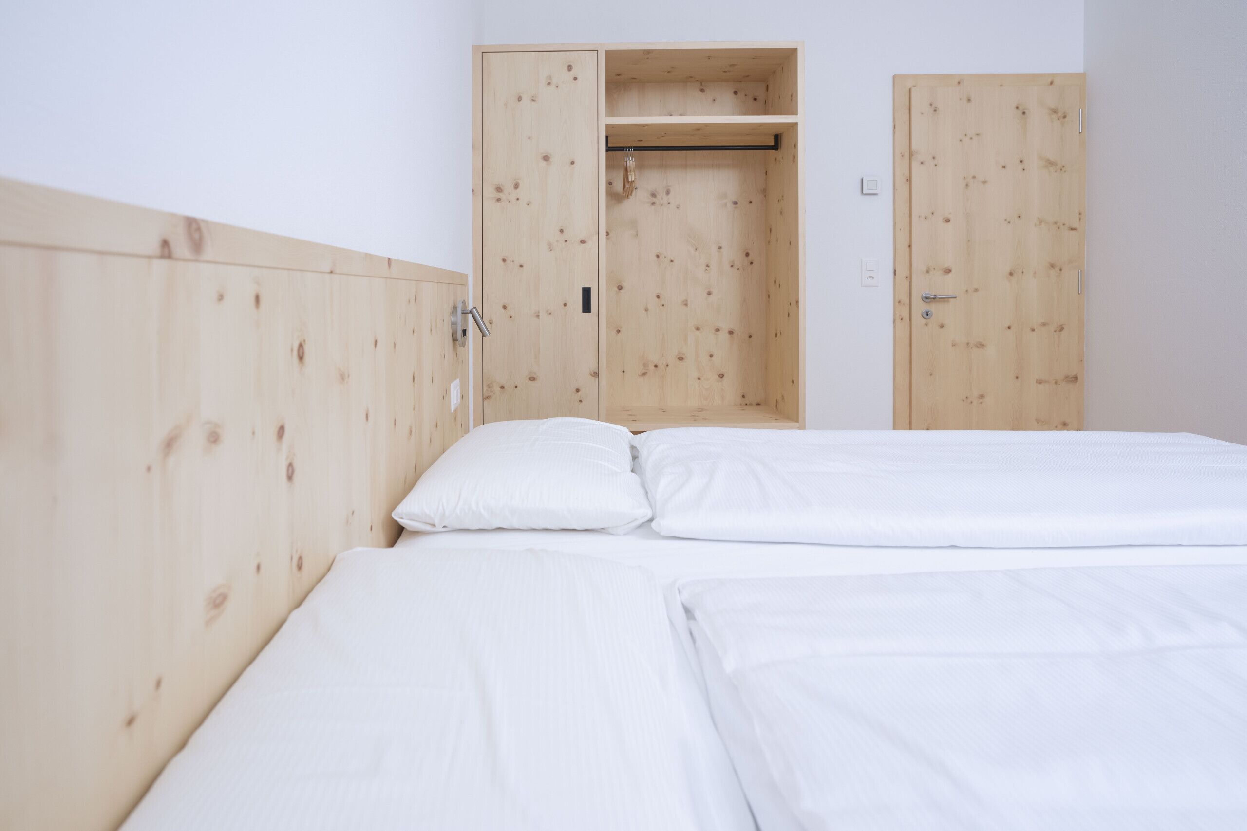 A room with a wooden wardrobe, a bed with white bedding, and a wooden headboard.