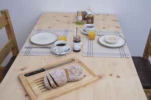 A wooden table set with breakfast items including a loaf of bread, a cup of coffee, a glass of orange juice, and a jar of jam. - Chasa Helvetia Studio: Relax and enjoy in the new studio with exclusive hotel service (Müstair)
