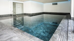 An indoor swimming pool with a clear water surface, a glass railing, and a tiled floor. - Chasa Helvetia Studio: Relax and enjoy in the new studio with exclusive hotel service (Müstair)