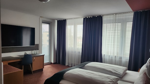 A hotel room with a bed, a desk, a chair, a television, and windows with curtains. - Eibacher Hof (Nuremberg)