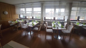 A dining area with multiple tables and chairs, large windows with sheer curtains, and a view of the outside. - Eibacher Hof (Nuremberg)