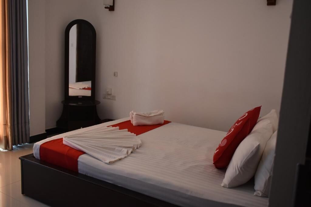 Een opgemaakt bed met witte en rode beddengoed, een rood kussen en een gevouwen handdoek aan de zijkant.