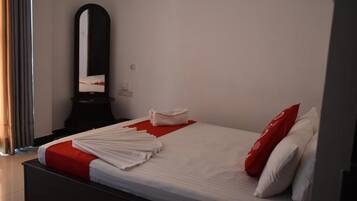 Een opgemaakt bed met witte en rode beddengoed, een rood kussen en een gevouwen handdoek aan de zijkant.