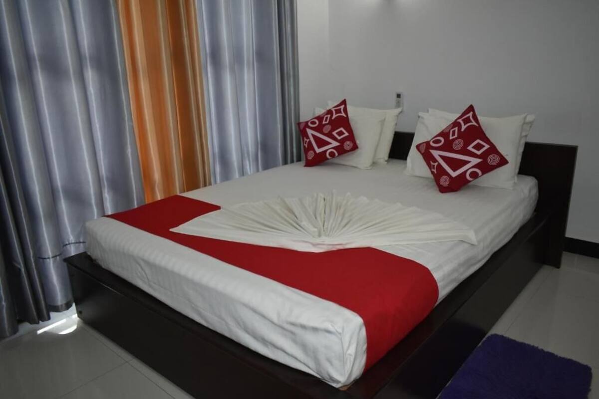 A neatly made bed with a red and white bedspread, two red pillows with white patterns, and a black headboard.