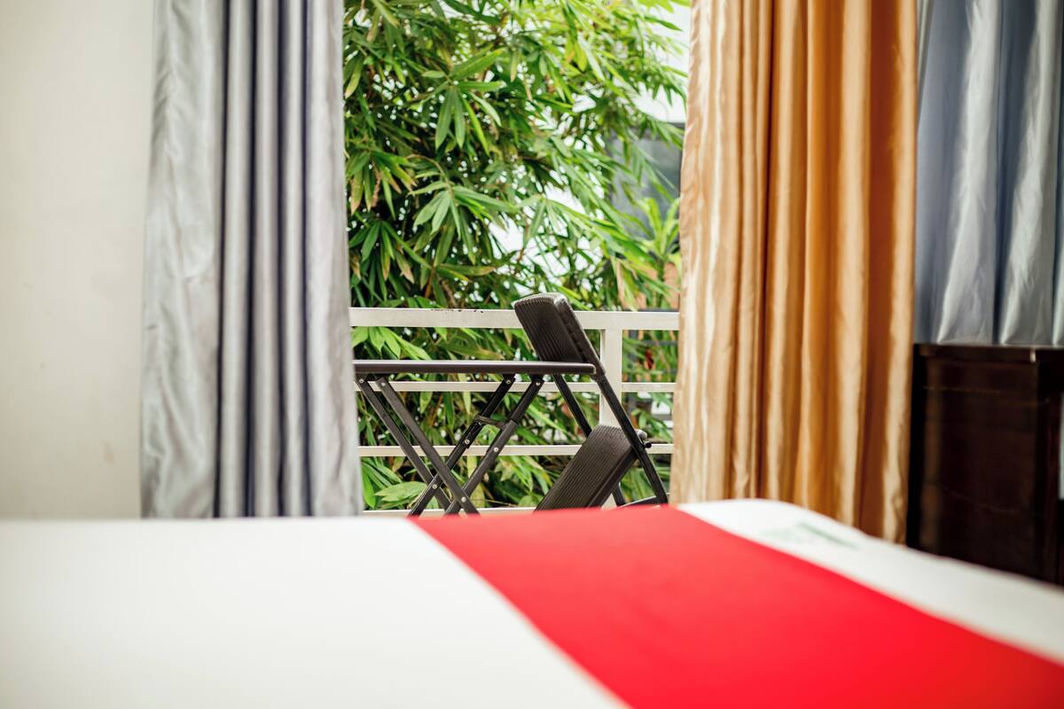 A room with a bed, a chair, and a view of greenery through curtains.