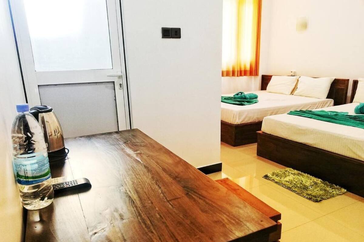 A hotel room with a wooden table, a remote control, a bottle of water, and two beds with green towels.