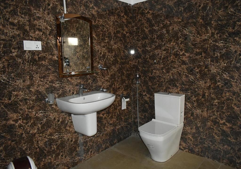 Uma casa de banho com parede de mármore, pia, espelho e sanita.
