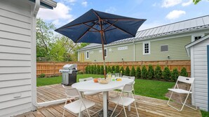A wooden deck with a white table and chairs, a barbecue grill, and a large umbrella.