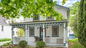 A two-story house with a porch, a small garden, and a blue door.