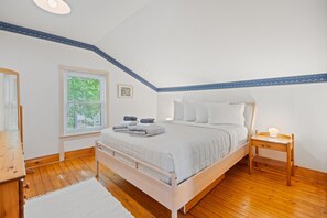 Een slaapkamer met een enkel bed, een nachtkastje, een raam met jaloezieën en een ingelijst foto aan de muur.