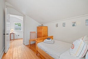 A bedroom with a wooden bed, a chair, a wooden wardrobe, and a small table with a lamp. - NEW! The Cedar House - Steps from Queen Street (Niagara-on-the-Lake)