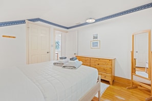 Une chambre à coucher avec un lit, une commode en bois, un miroir et une porte.