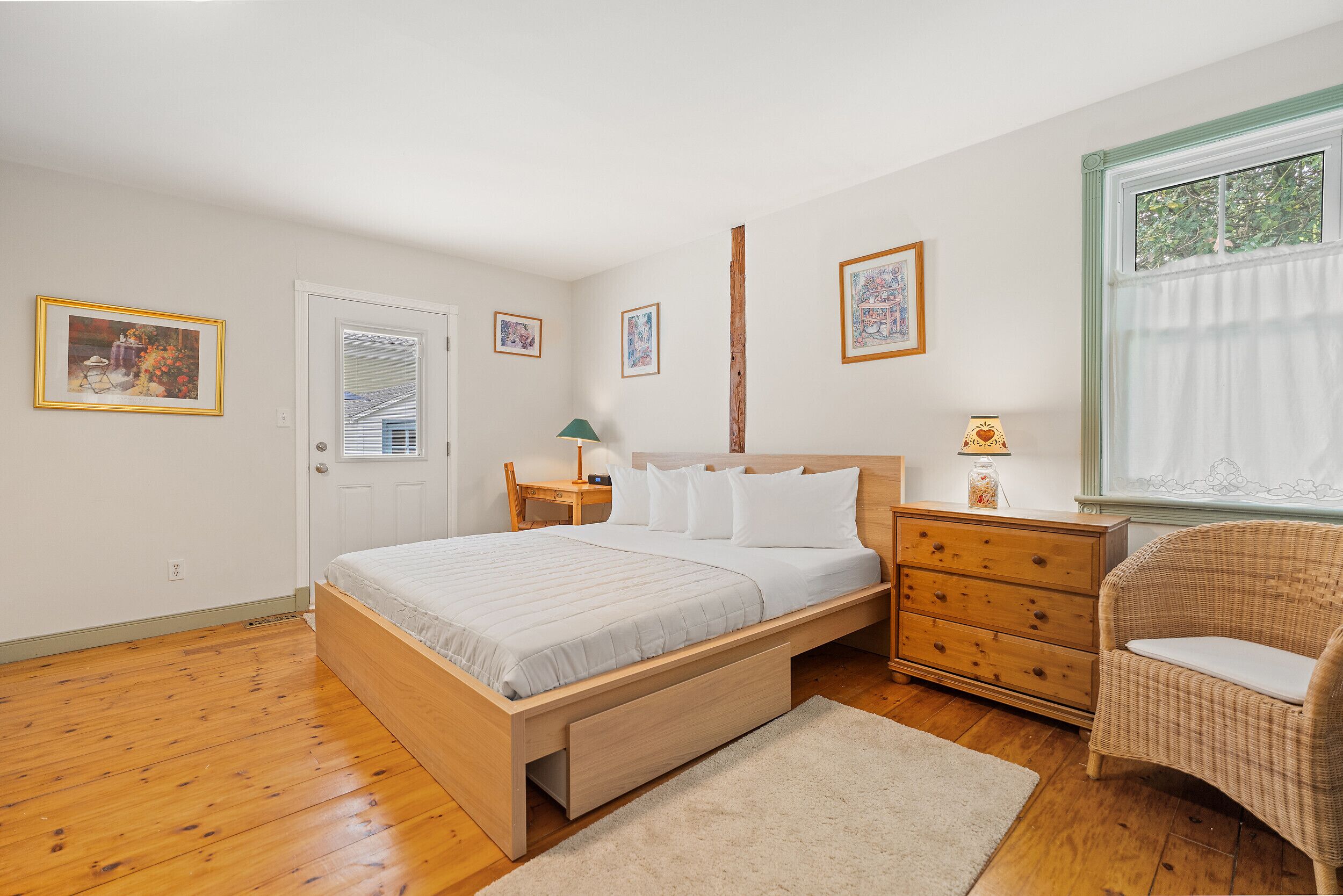 Une chambre à coucher avec un lit en bois, une table de chevet, une commode, une chaise et des tableaux encadrés accrochés au mur.