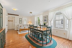 Un comedor con mesa y sillas de madera, un sofá y una ventana con cortinas blancas.