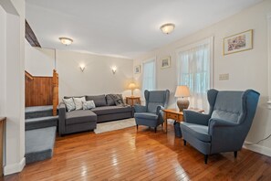 A living room with a grey sofa, a blue armchair, a wooden staircase, and a wooden floor. - The Cedar House - Steps from Queen Street (Niagara-on-the-Lake)