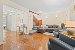Amplia sala de estar con escalera de madera, un sofá modular gris y una mesita con lámpara.
