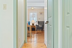A hallway leading to a living room with a lamp, chair, and a framed picture on the wall. - NEW! The Cedar House - Steps from Queen Street (Niagara-on-the-Lake)