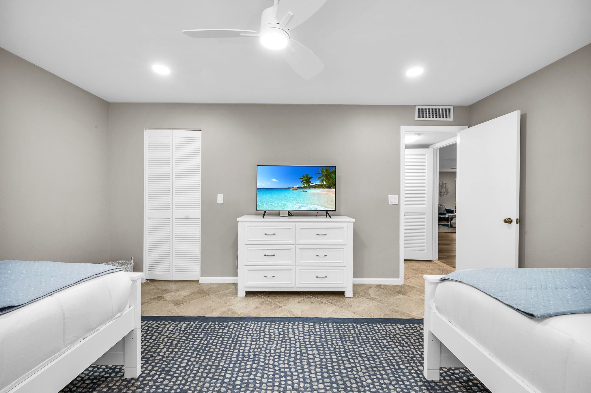 A bedroom with two beds, a TV on a dresser, a ceiling fan, and a closet.